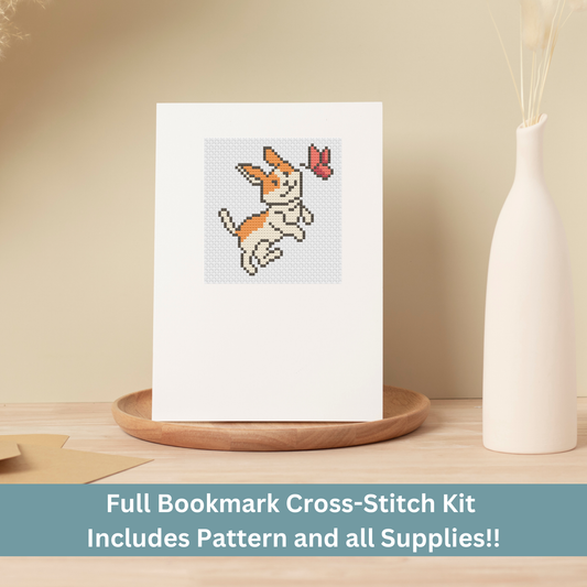 Cross-stitch greeting card featuring an orange and white dog chasing a butterfly, stitched on Aida cloth.