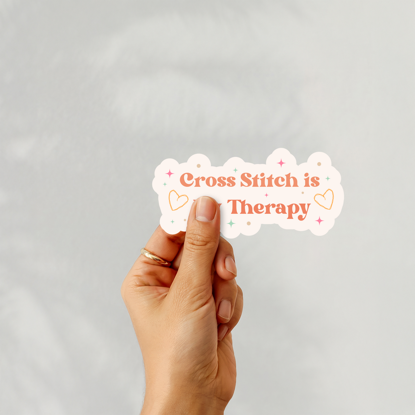 Hand holding “Cross Stitch is My Therapy” sticker with hearts and pastel details