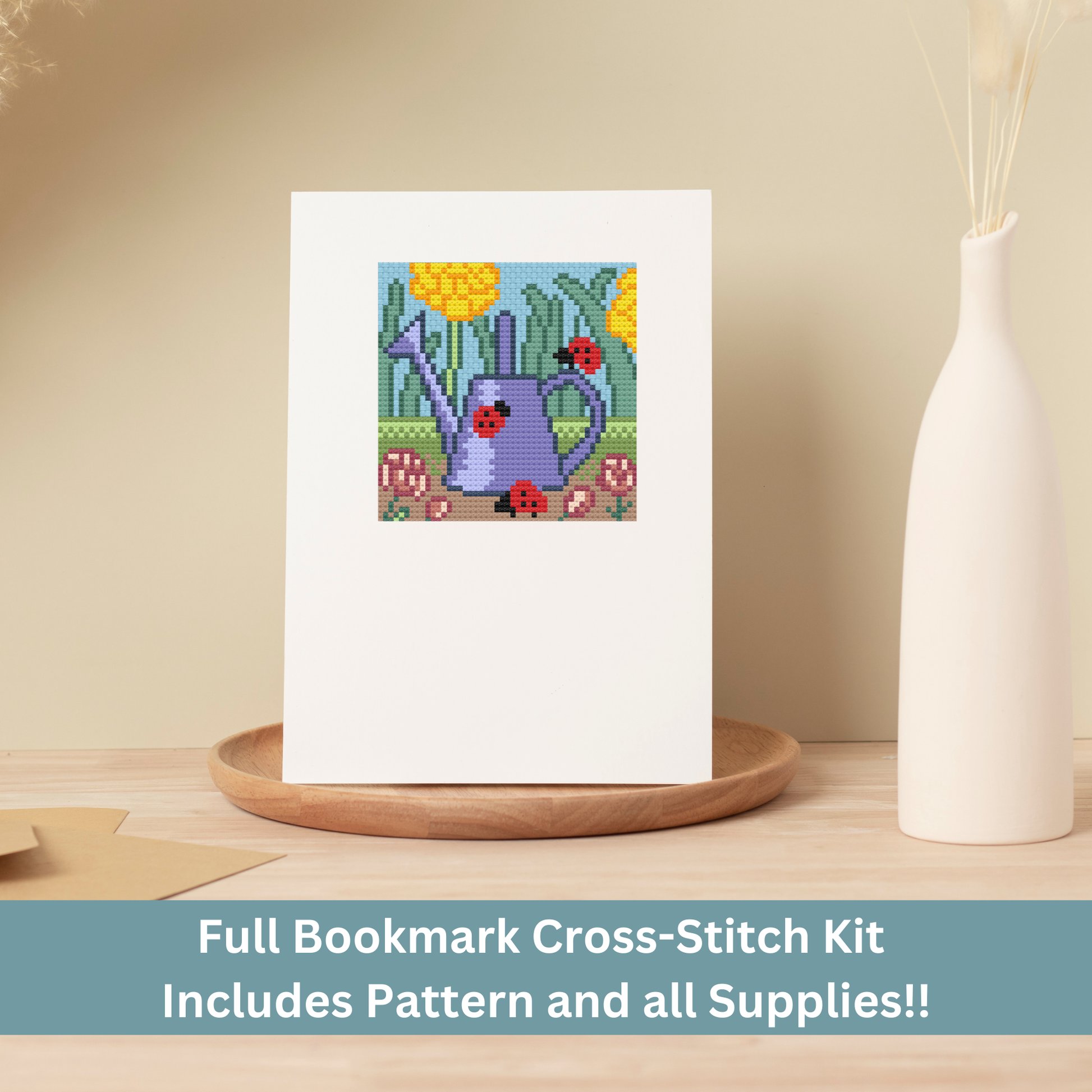 Cross-stitch greeting card featuring a purple watering can with ladybugs and yellow flowers, stitched on Aida cloth.